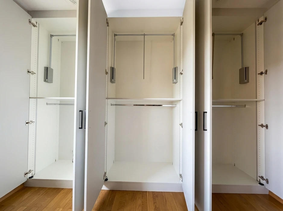 Armoire encastrée blanche ouverte, trois colonnes avec portes battantes à charnières invisibles et poignées noires