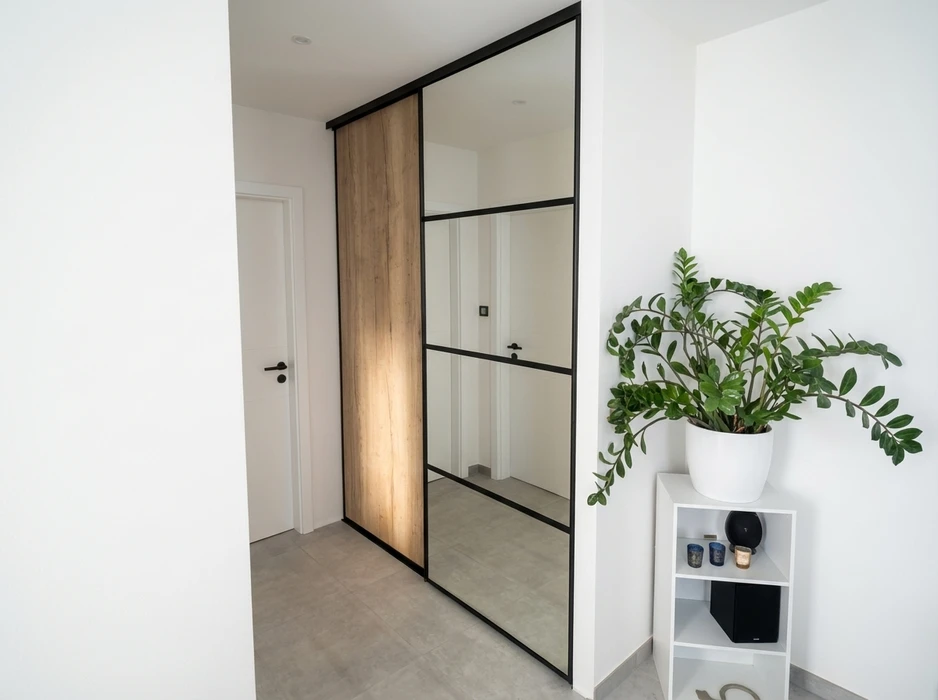 Couloir d'entrée moderne avec armoire encastrée à portes coulissantes : un panneau en bois chêne naturel et deux portes miroir à cadre noir mat