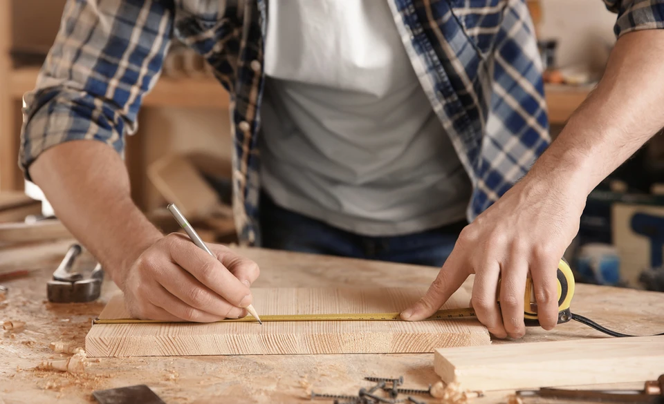Atelier de menuiserie avec artisan en tablier de cuir consultant un carnet technique tout en inspectant des planches de bois brut