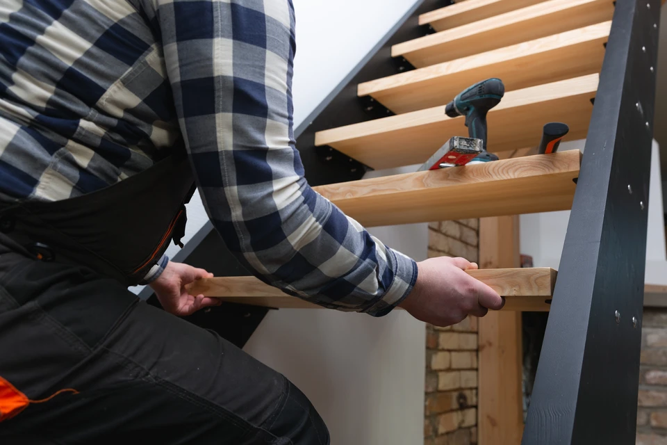 Atelier de menuiserie intérieur avec artisan en vêtements de travail gris mesurant une planche de bois avec un mètre ruban